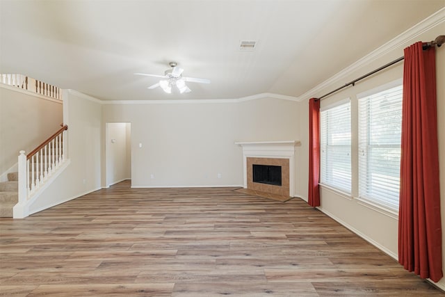 unfurnished living room featuring crown molding, light wood finished floors, visible vents, a tile fireplace, and stairs