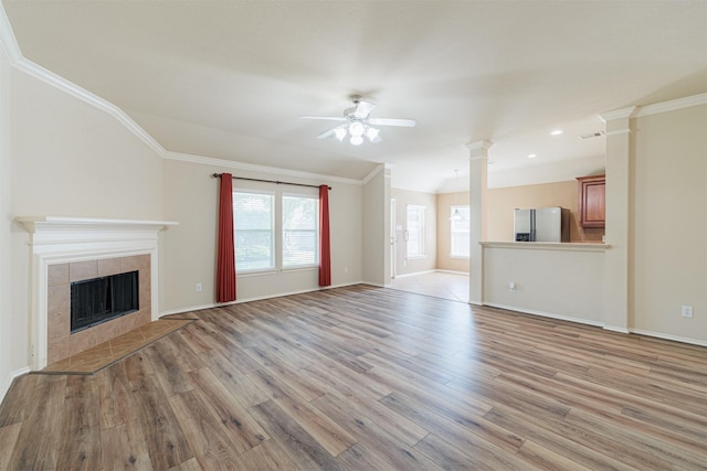 unfurnished living room featuring ornamental molding, ceiling fan, light wood-type flooring, ornate columns, and a tile fireplace