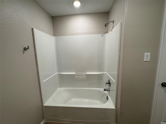 bathroom with a textured wall and shower / bathtub combination