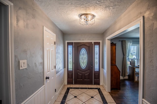 foyer with a textured ceiling, a textured wall, and a wainscoted wall