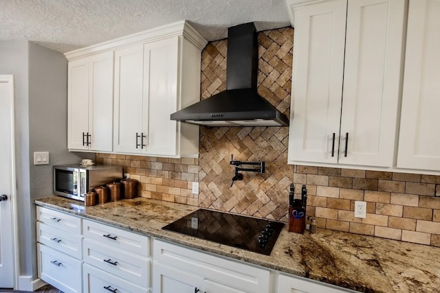 kitchen featuring wall chimney exhaust hood, black electric stovetop, stainless steel microwave, decorative backsplash, and white cabinetry