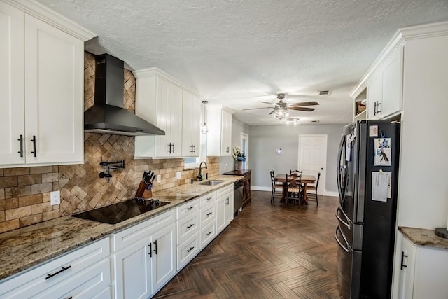 kitchen featuring black appliances, wall chimney exhaust hood, a ceiling fan, white cabinetry, and backsplash
