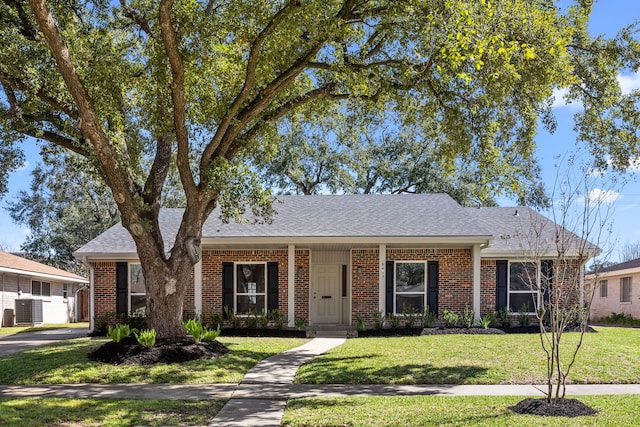 single story home with a shingled roof, a front yard, brick siding, and central AC unit