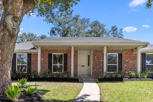 ranch-style home with a shingled roof, a front yard, and brick siding