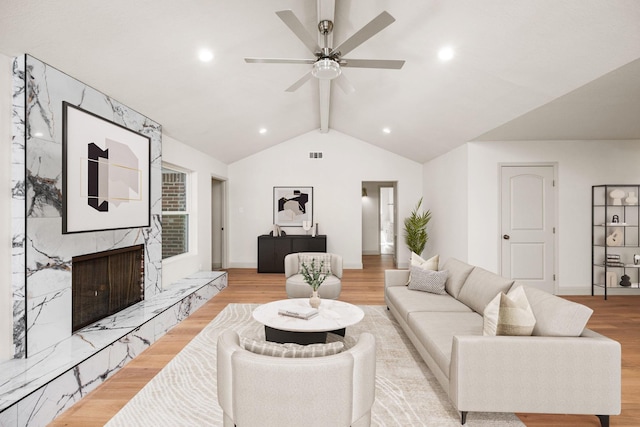 living area with visible vents, baseboards, vaulted ceiling with beams, light wood-type flooring, and a high end fireplace