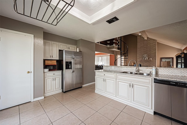 kitchen with light tile patterned floors, cream cabinets, a sink, appliances with stainless steel finishes, and tasteful backsplash