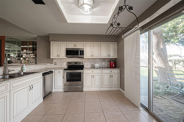 kitchen featuring light tile patterned floors, tasteful backsplash, a raised ceiling, stainless steel appliances, and a sink