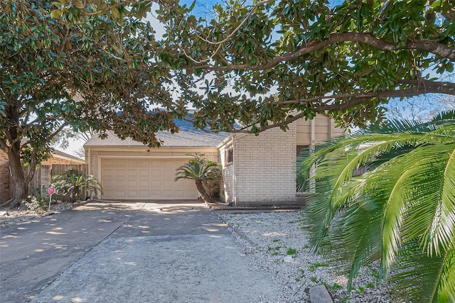 view of property hidden behind natural elements featuring brick siding, driveway, an attached garage, and fence