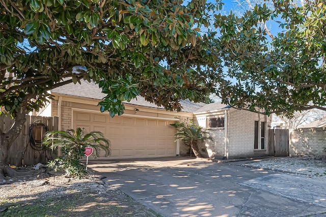 view of front facade featuring driveway, brick siding, an attached garage, and fence