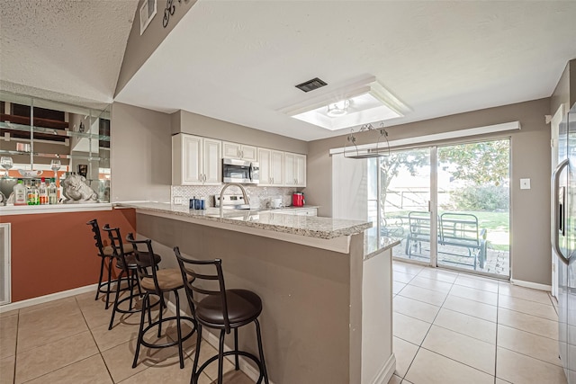 kitchen with light tile patterned flooring, stainless steel appliances, visible vents, decorative backsplash, and a kitchen bar