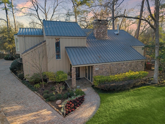 view of front of property with a standing seam roof, a chimney, a front lawn, stone siding, and metal roof