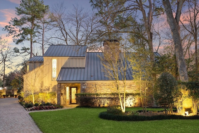 view of front of house with stone siding, a chimney, metal roof, a standing seam roof, and a front yard