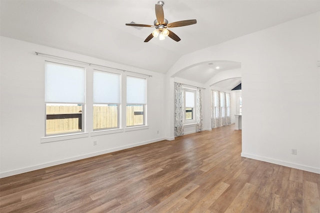 empty room with vaulted ceiling, arched walkways, wood finished floors, and baseboards