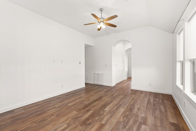 empty room featuring arched walkways, a ceiling fan, vaulted ceiling, wood finished floors, and baseboards