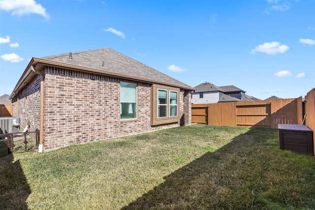 back of property featuring brick siding, a lawn, a fenced backyard, and roof with shingles