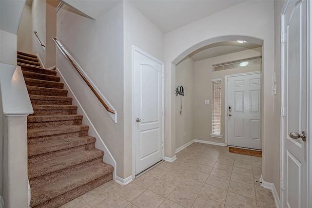 foyer with arched walkways, light tile patterned floors, stairway, and baseboards