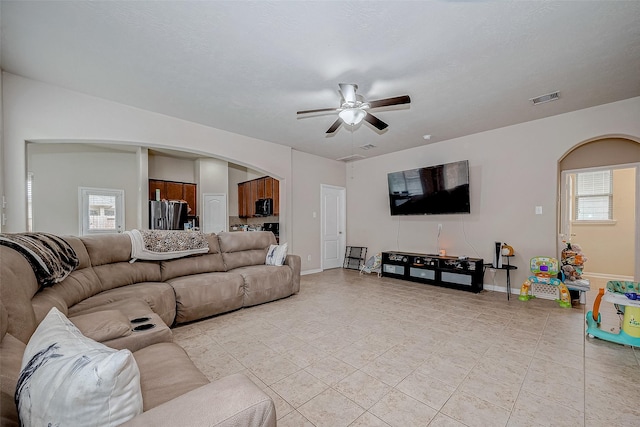 living area with arched walkways, ceiling fan, light tile patterned floors, visible vents, and baseboards