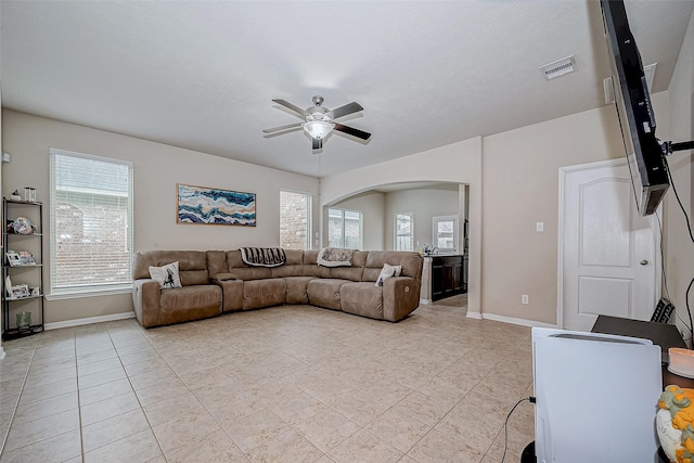 living room featuring arched walkways, light tile patterned floors, visible vents, a ceiling fan, and baseboards