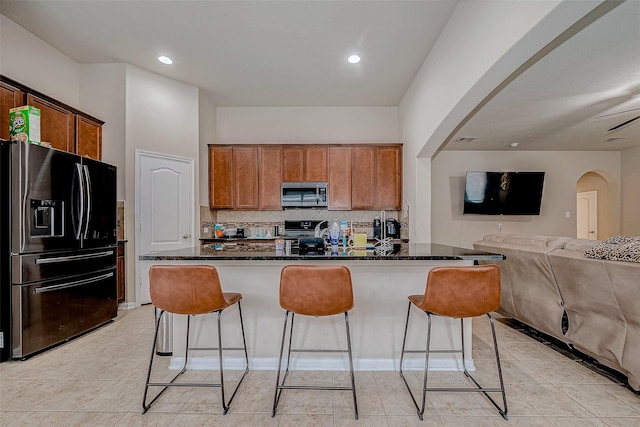 kitchen with tasteful backsplash, dark stone counters, a breakfast bar, open floor plan, and stainless steel appliances