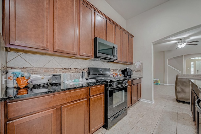 kitchen with arched walkways, black gas range oven, stainless steel microwave, dark stone countertops, and light tile patterned flooring