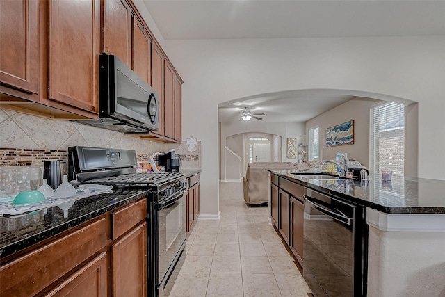 kitchen with arched walkways, light tile patterned floors, a ceiling fan, black appliances, and dark stone countertops