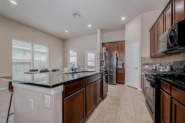 kitchen featuring stainless steel refrigerator with ice dispenser, visible vents, black gas range, a sink, and dark stone countertops