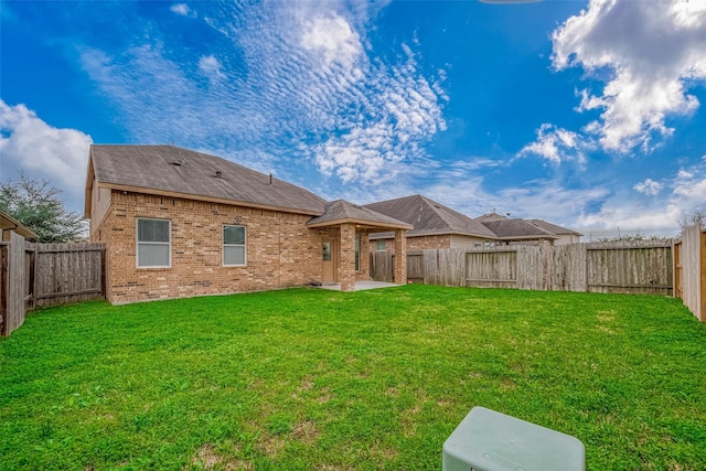 back of house with a patio area, a fenced backyard, a lawn, and brick siding