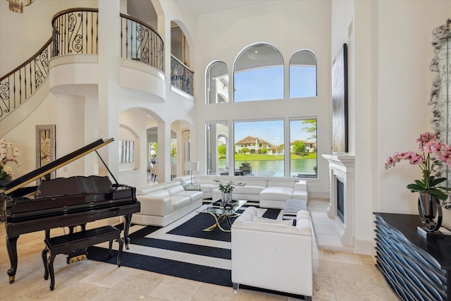 living room featuring arched walkways, a fireplace with raised hearth, a towering ceiling, stairway, and tile patterned floors