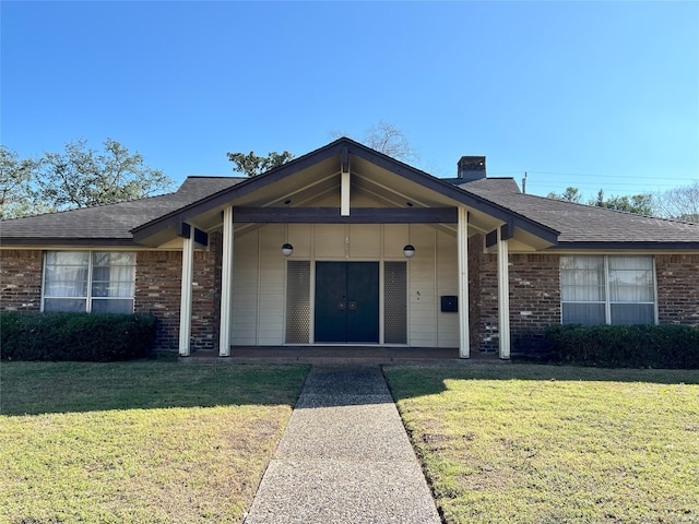 ranch-style home with a shingled roof, a front yard, brick siding, and a chimney