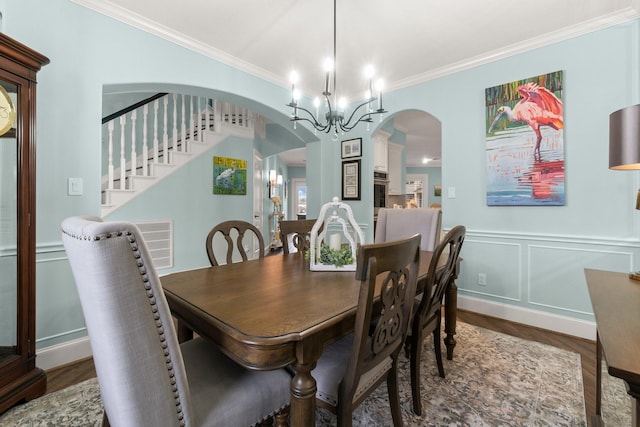 dining area with arched walkways, a decorative wall, wood finished floors, an inviting chandelier, and crown molding