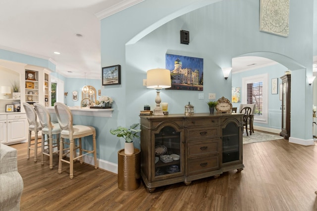 interior space with ornamental molding, arched walkways, baseboards, and wood finished floors