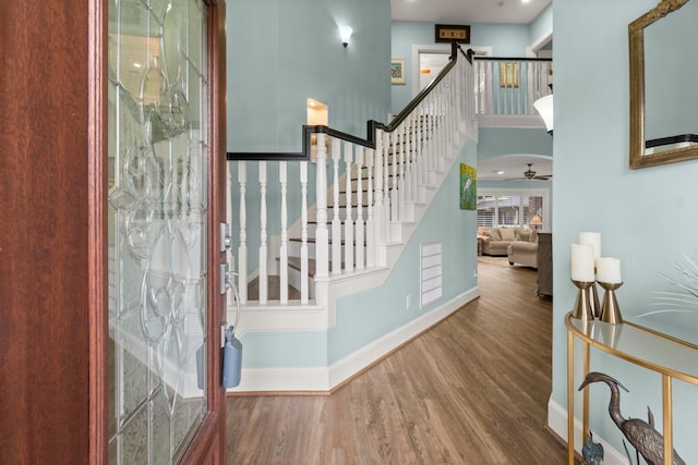 staircase featuring arched walkways, a high ceiling, a ceiling fan, wood finished floors, and baseboards