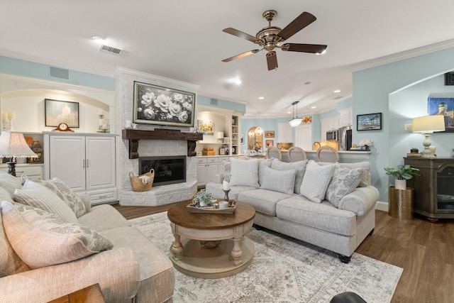 living area with a fireplace, wood finished floors, visible vents, and crown molding