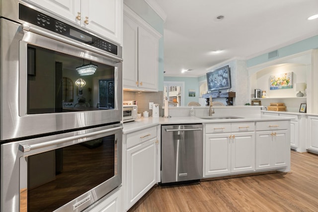 kitchen with a sink, white cabinetry, appliances with stainless steel finishes, light wood-type flooring, and tasteful backsplash