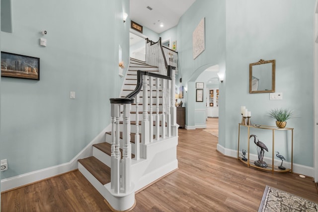 stairway with arched walkways, wood finished floors, a towering ceiling, and baseboards