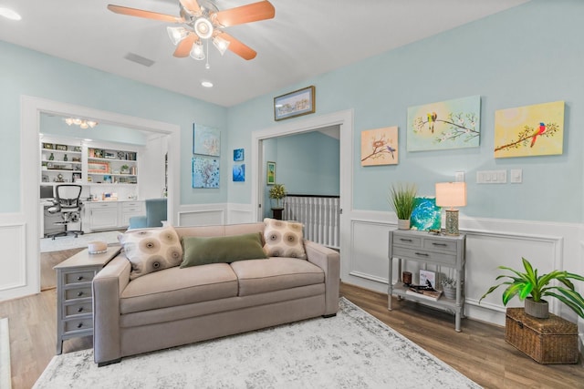 living area with built in shelves, visible vents, wainscoting, ceiling fan, and wood finished floors