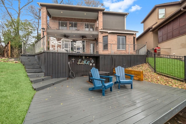 wooden terrace with a ceiling fan, fence, stairway, and a lawn