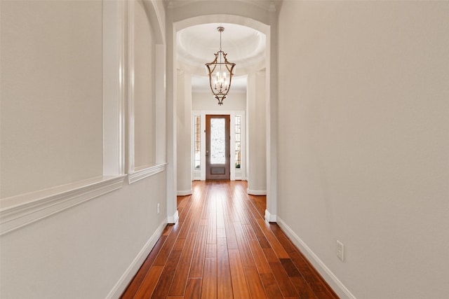 corridor with baseboards, arched walkways, dark wood finished floors, crown molding, and a notable chandelier