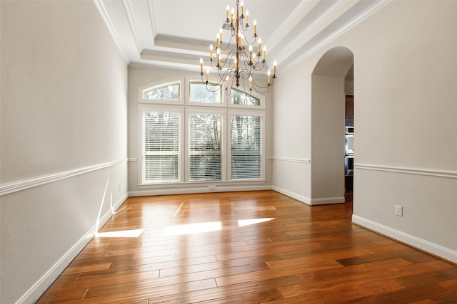 unfurnished dining area featuring arched walkways, crown molding, a raised ceiling, wood finished floors, and baseboards