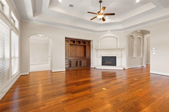 unfurnished living room with hardwood / wood-style flooring, arched walkways, and a raised ceiling