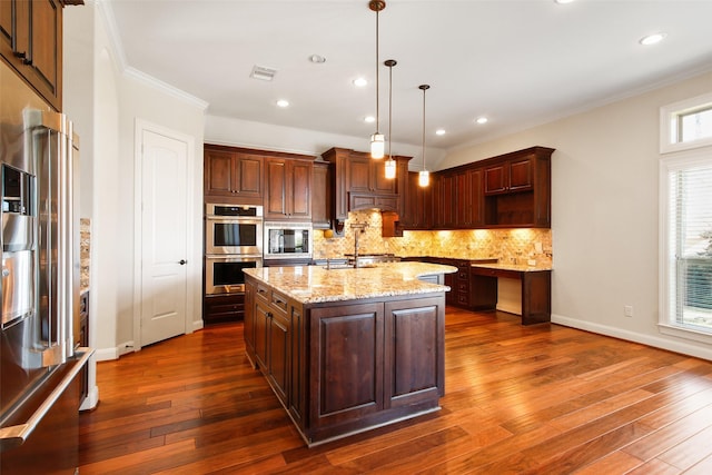 kitchen featuring a center island with sink, stainless steel appliances, backsplash, dark wood-type flooring, and ornamental molding