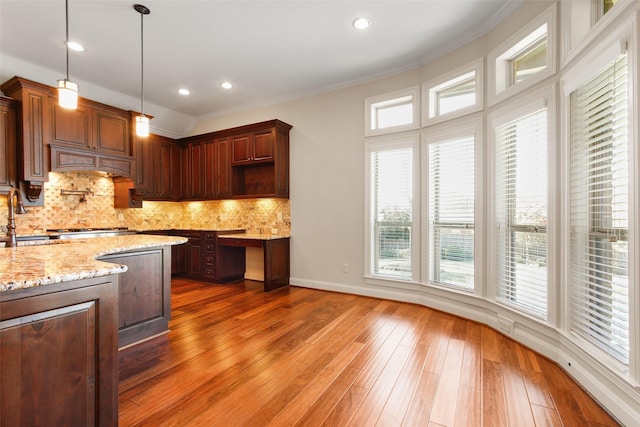 kitchen featuring a sink, hanging light fixtures, ornamental molding, backsplash, and wood-type flooring