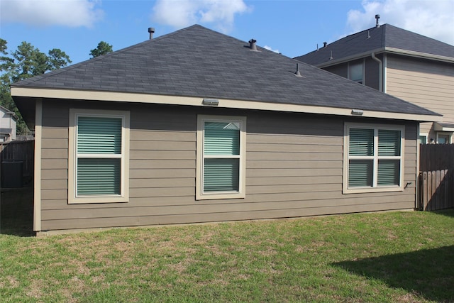 view of side of home with a shingled roof, a lawn, and fence