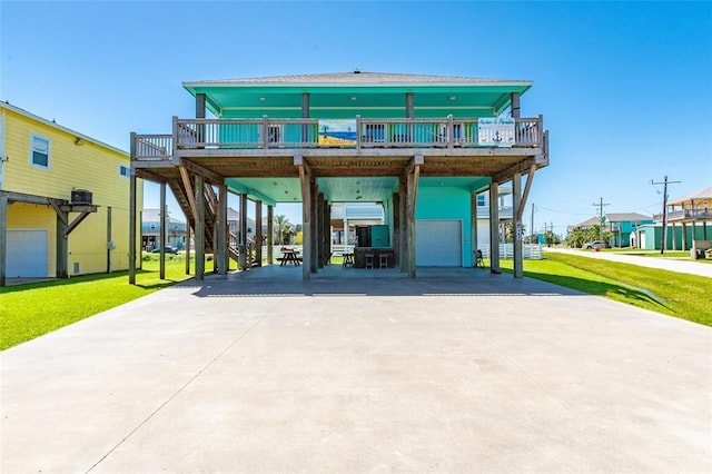 back of house featuring a deck, an attached garage, driveway, a lawn, and a carport