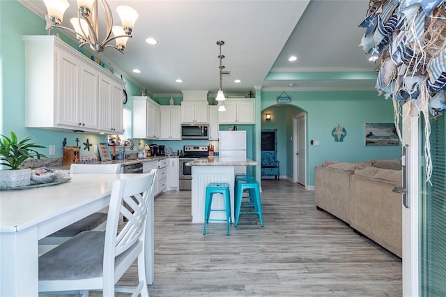 kitchen with arched walkways, a breakfast bar, stainless steel appliances, open floor plan, and white cabinetry