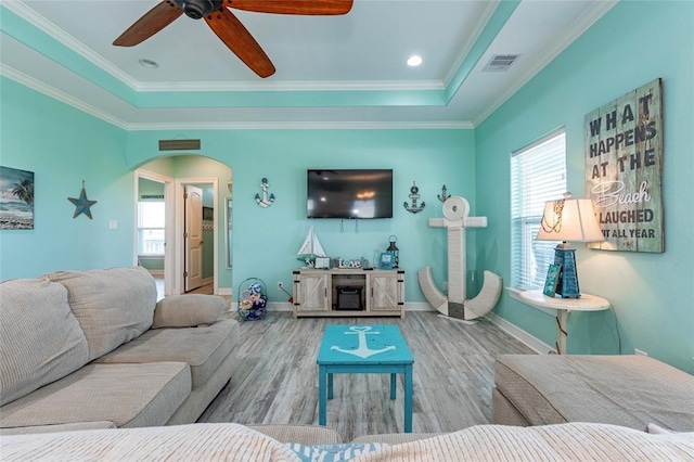 living room featuring arched walkways, a tray ceiling, crown molding, visible vents, and wood finished floors