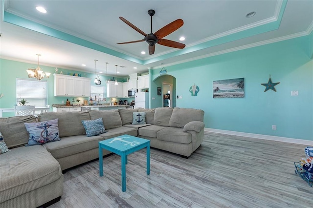 living room featuring arched walkways, ceiling fan with notable chandelier, baseboards, a tray ceiling, and crown molding