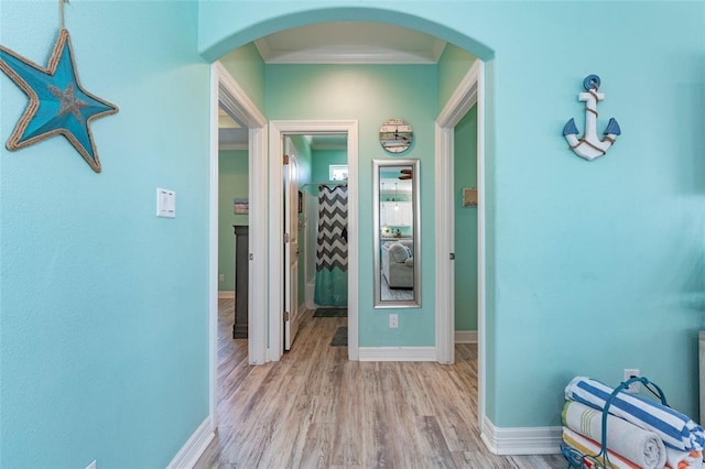 hallway with baseboards, light wood-type flooring, arched walkways, and crown molding