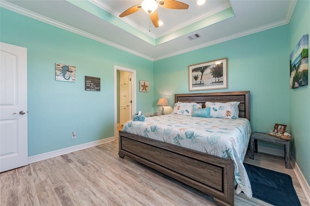 bedroom with baseboards, visible vents, a raised ceiling, ornamental molding, and wood finished floors