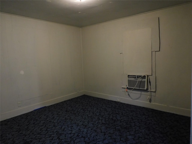 unfurnished room with a wall unit AC, baseboards, and dark carpet